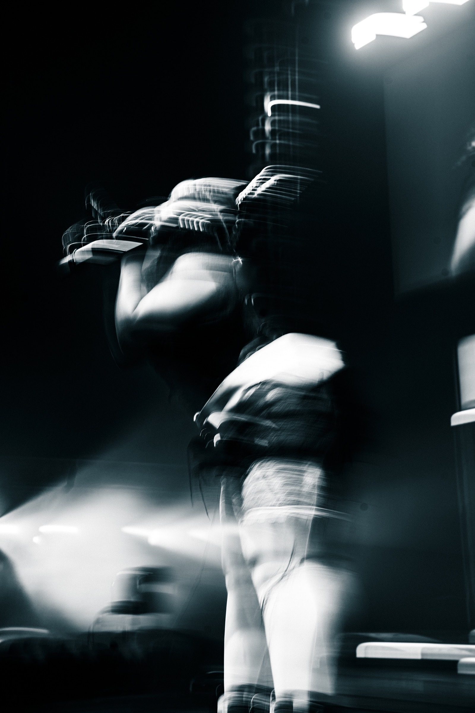 Noir et blanc en pose longue, une silhouette en mouvement sur scène, traînées de lumière blanche.